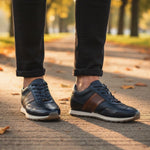 bugatti Ivar dark blue leather sneakers with brown stripe, white midsole, worn with black jeans.
