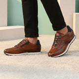 Lifestyle shot of brown leather bugatti sneakers with black laces and dark blue accent, worn with black pants.
