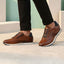 Lifestyle shot of brown leather bugatti sneakers with black laces and dark blue accent, worn with black pants.
