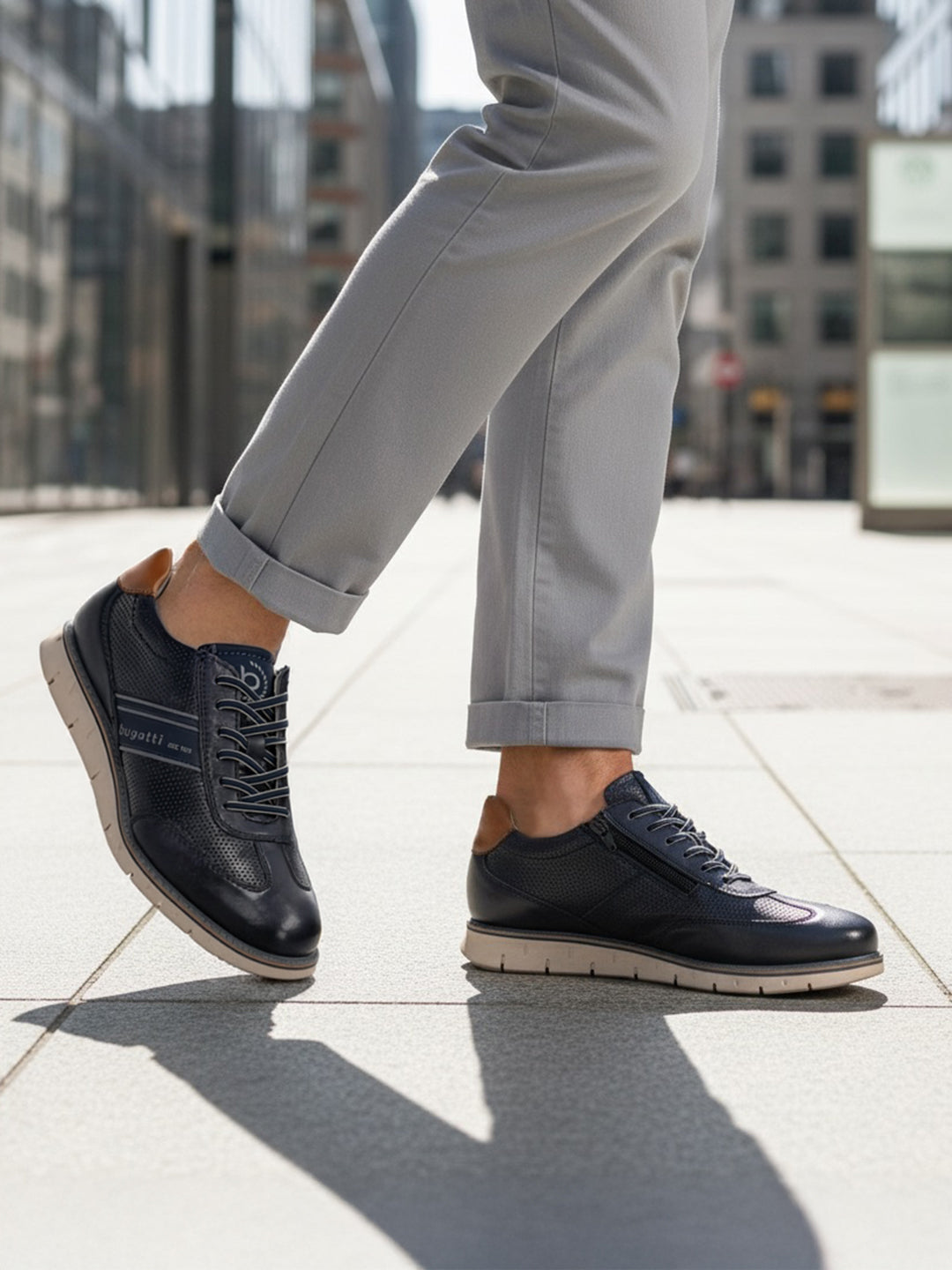 Lifestyle shot of bugatti Sprinter dark blue leather sneakers with light soles, paired with gray casual pants.
