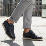Lifestyle shot of bugatti Sprinter dark blue leather sneakers with light soles, paired with gray casual pants.
