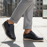 Lifestyle shot of bugatti Sprinter dark blue leather sneakers with light soles, paired with gray casual pants.

