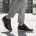 Lifestyle shot of bugatti Sprinter dark blue leather sneakers with light soles, paired with gray casual pants.
