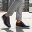 Lifestyle shot of bugatti Sprinter dark blue leather sneakers with light soles, paired with gray casual pants.
