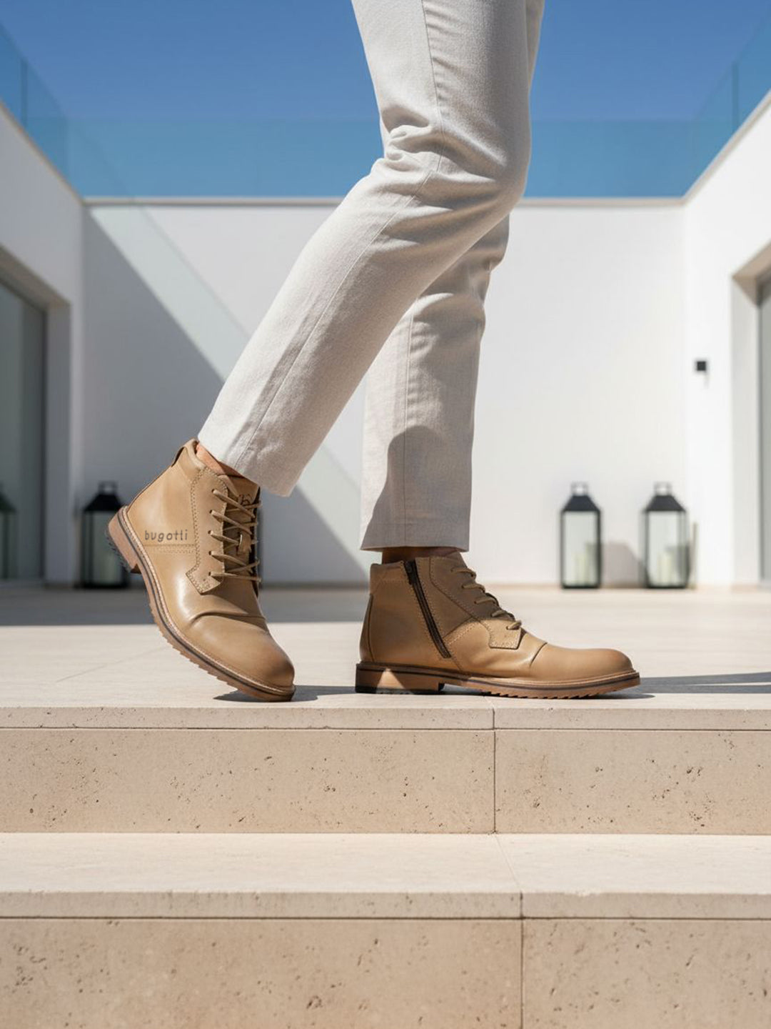 Lifestyle shot of Bugatti Baldor boots in sand-colored leather, featuring a side zipper and lace-up closure, paired with light-colored trousers.

