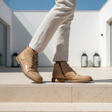 Lifestyle shot of Bugatti Baldor boots in sand-colored leather, featuring a side zipper and lace-up closure, paired with light-colored trousers.
