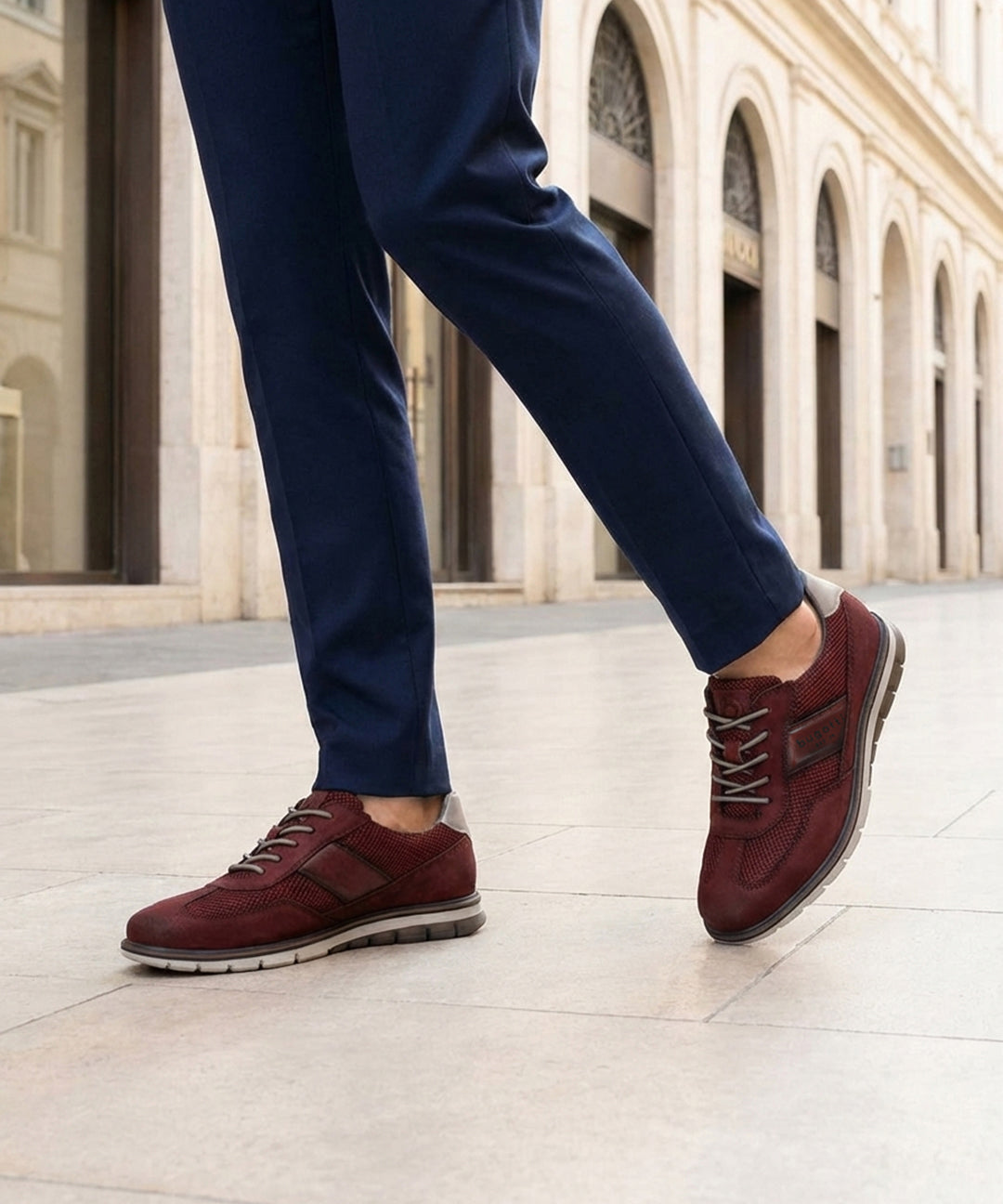 Cropped lifestyle image of bugatti Simone Comfort dark red leather casual shoes with grey soles, worn with blue trousers.
