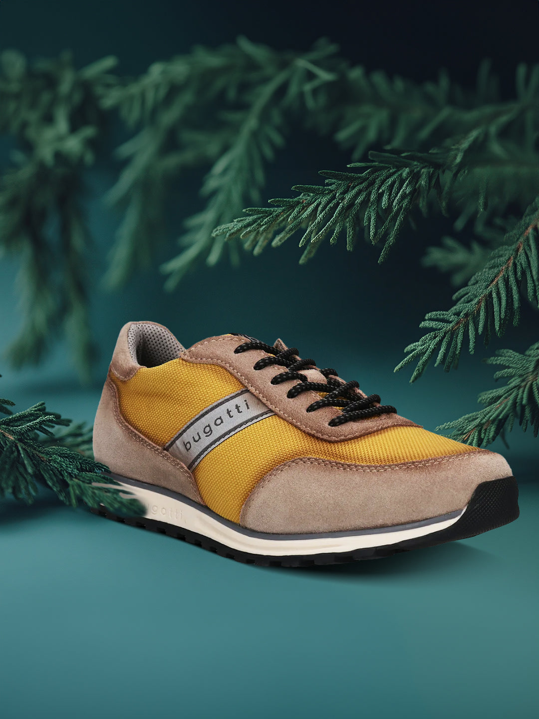 Taupe and yellow sneaker by bugatti, with black laces, styled with dark green conifer branches.
