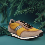 Taupe and yellow sneaker by bugatti, with black laces, styled with dark green conifer branches.
