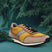 Taupe and yellow sneaker by bugatti, with black laces, styled with dark green conifer branches.
