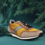 Taupe and yellow sneaker by bugatti, with black laces, styled with dark green conifer branches.

