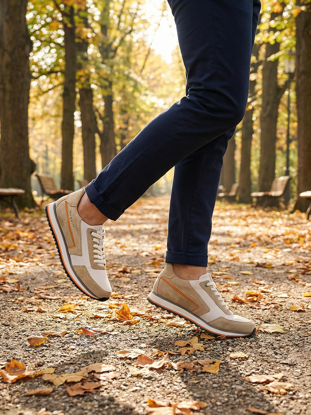Lifestyle shot of bugatti Garnet Evo Sand sneakers in leather and suede, styled with navy trousers while walking on a path.