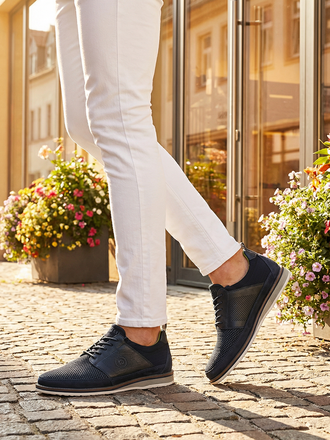 Lifestyle close-up of bugatti Sione Comfort dark blue casual shoes worn with white pants.
