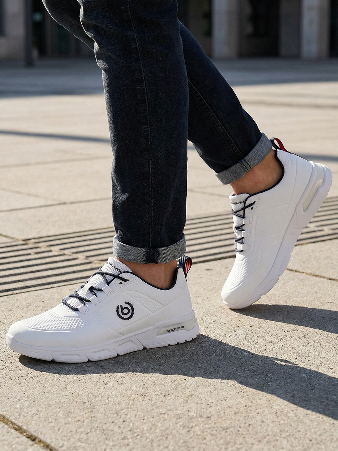 Lifestyle shot of the bugatti Nubola white sneakers, featuring black laces and logo detail, paired with dark denim jeans.
