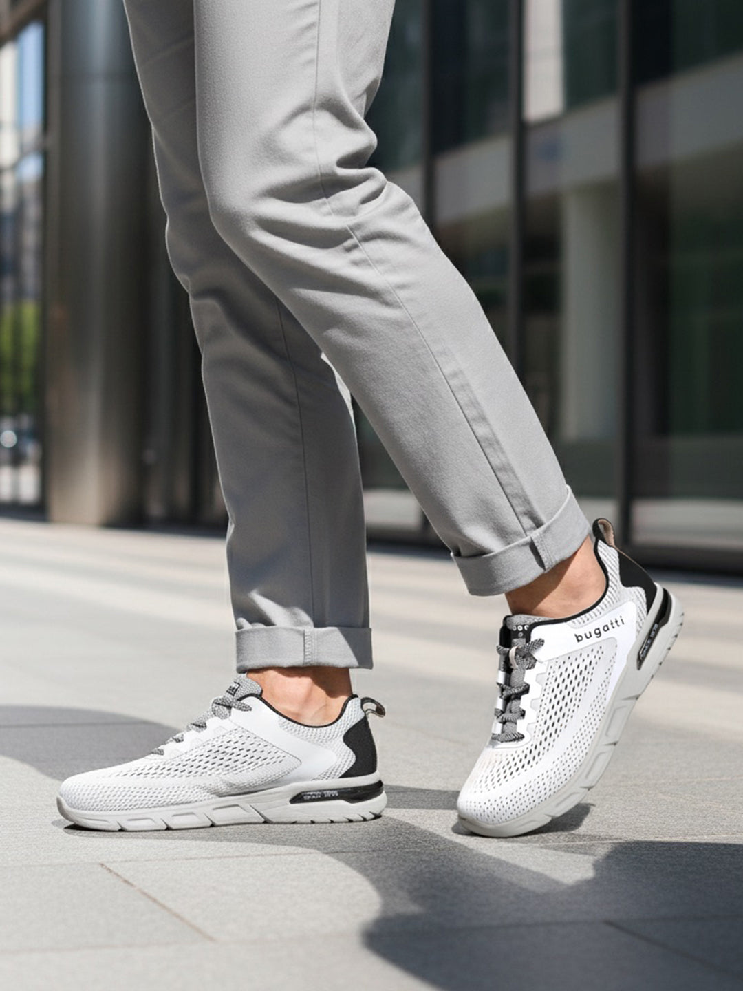 Cropped lifestyle shot of bugatti Nubola white sneakers with gray soles, black accents, and gray laces, worn with gray pants.