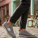 Grey low top sneakers by bugatti with a knit texture and white accent stripes, worn with dark grey pants.