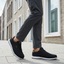 bugatti Baldini black sneakers, side view; low-cut with a white sole, worn with gray dress pants.