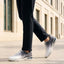 Cropped lifestyle view of bugatti Nubola white athleisure sneakers with a gradient design and white soles, worn with black trousers.
