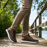 Brown and tan comfort casual boots by Bugatti, styled with a white midsole and worn with khaki trousers on a wooden boardwalk.
