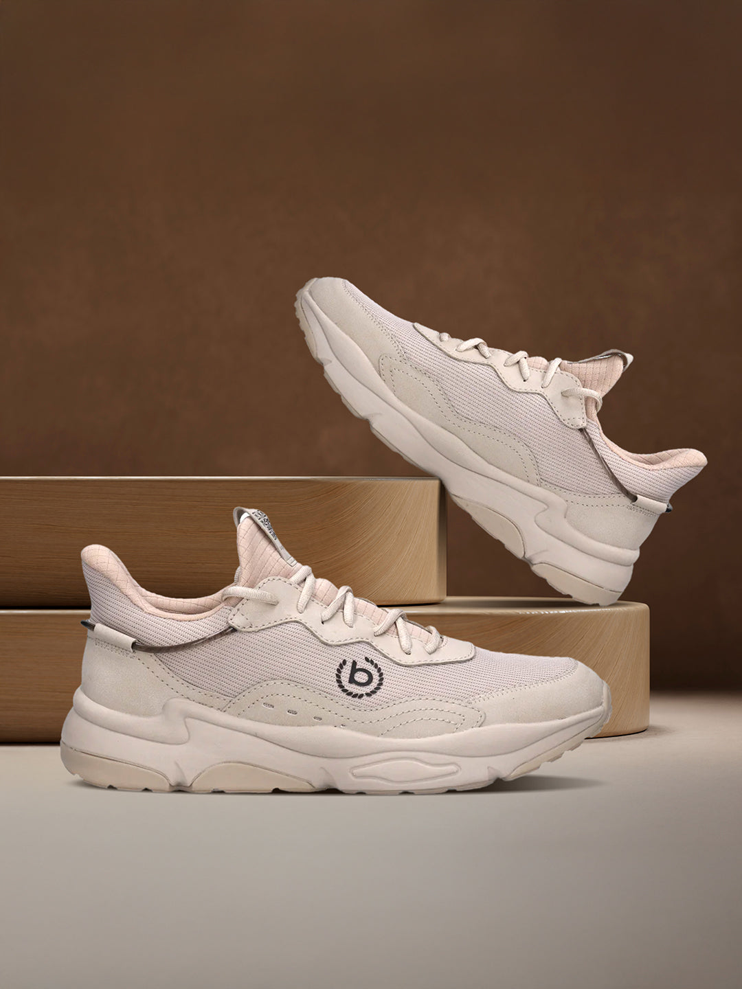 Beige bugatti Adelson Comfort Sneakers with breathable mesh and synthetic suede, presented on wooden display blocks.
